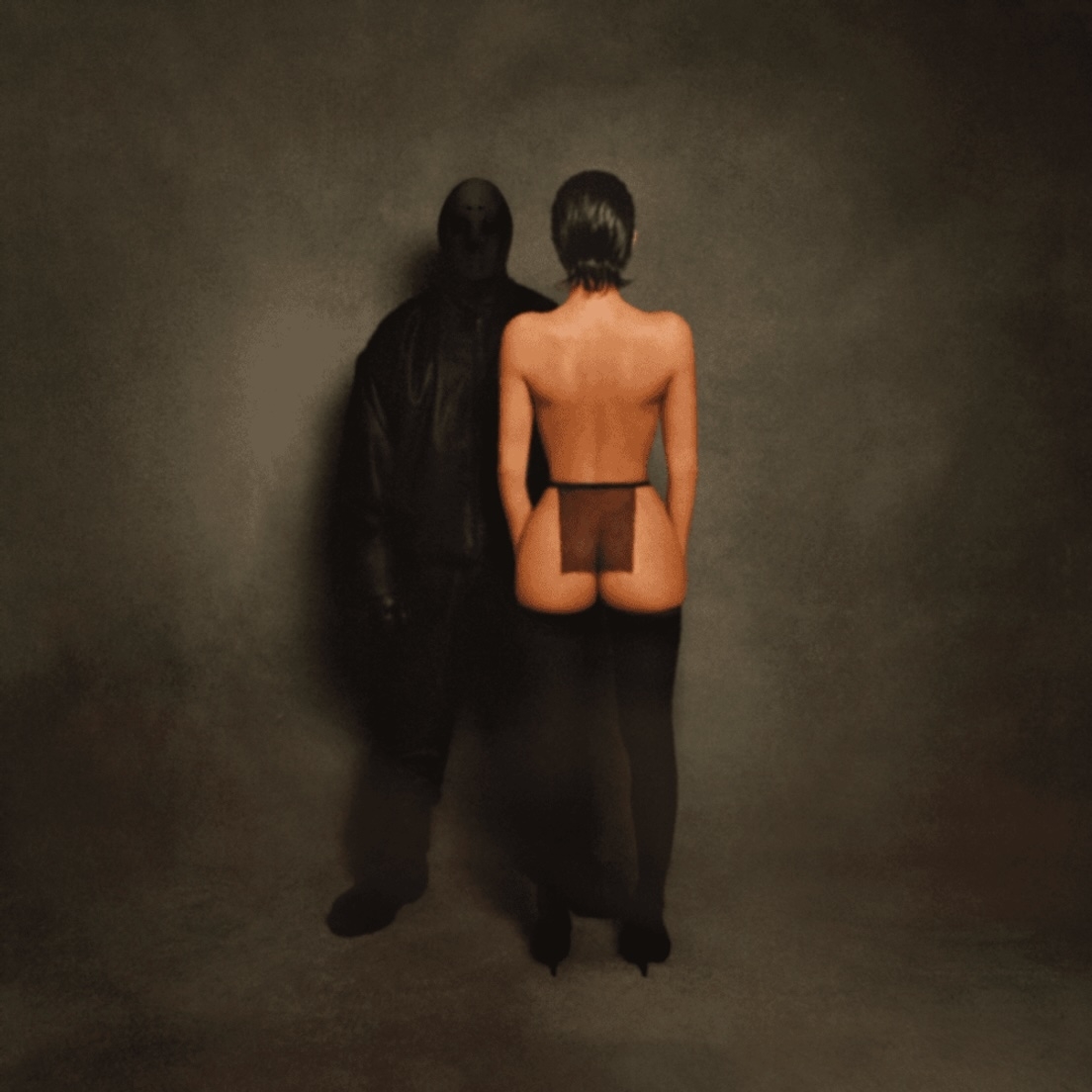 Two figures stand in a shadowy setting. One, dressed in black, faces forward. The other, wearing revealing attire, faces away from the camera