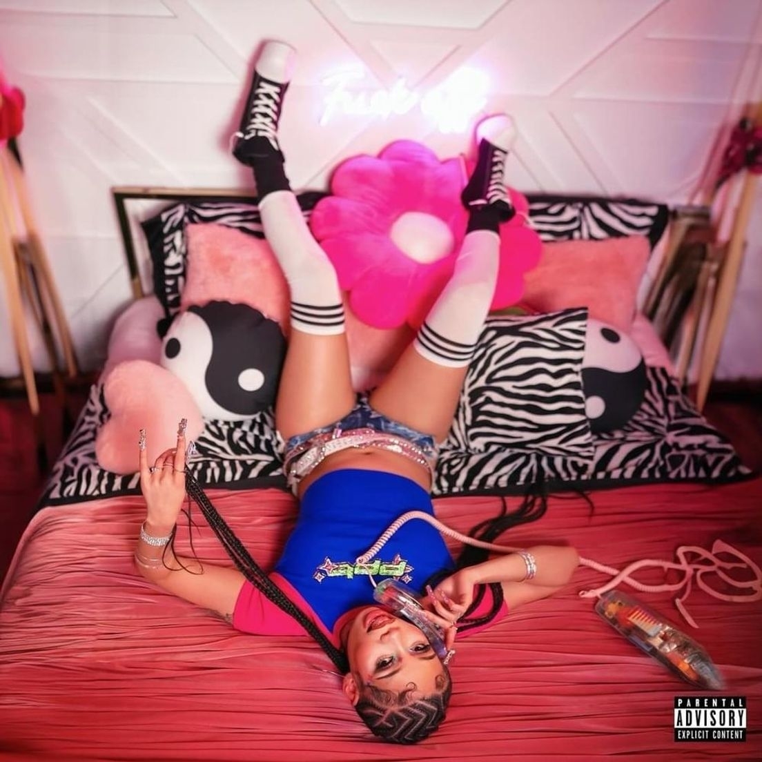 Young female musician in a playful pose on a bed with zebra print sheets, wearing a blue top, shorts, thigh-high socks, and platform sneakers. Neon sign above her