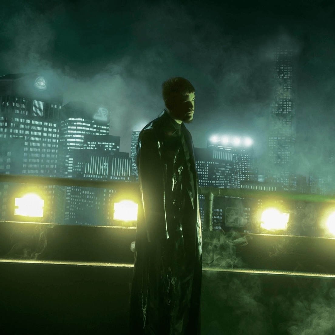 Person in dark trench coat stands on a rooftop with a misty city skyline and illuminated buildings in the background
