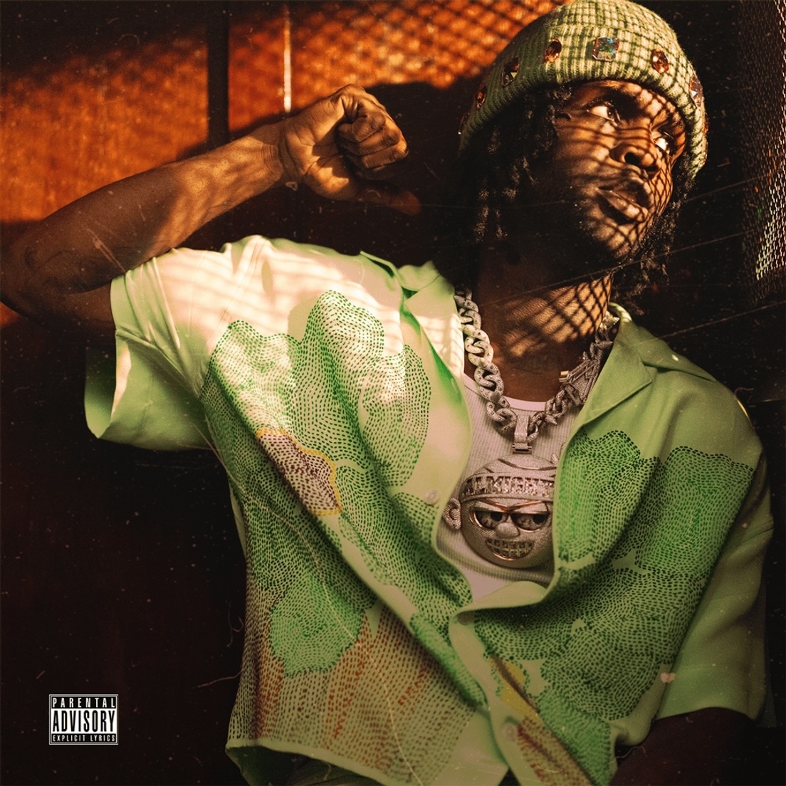Young Nudy poses in a green shirt, wearing a chunky chain and knitted hat, with a Parental Advisory sticker on the image
