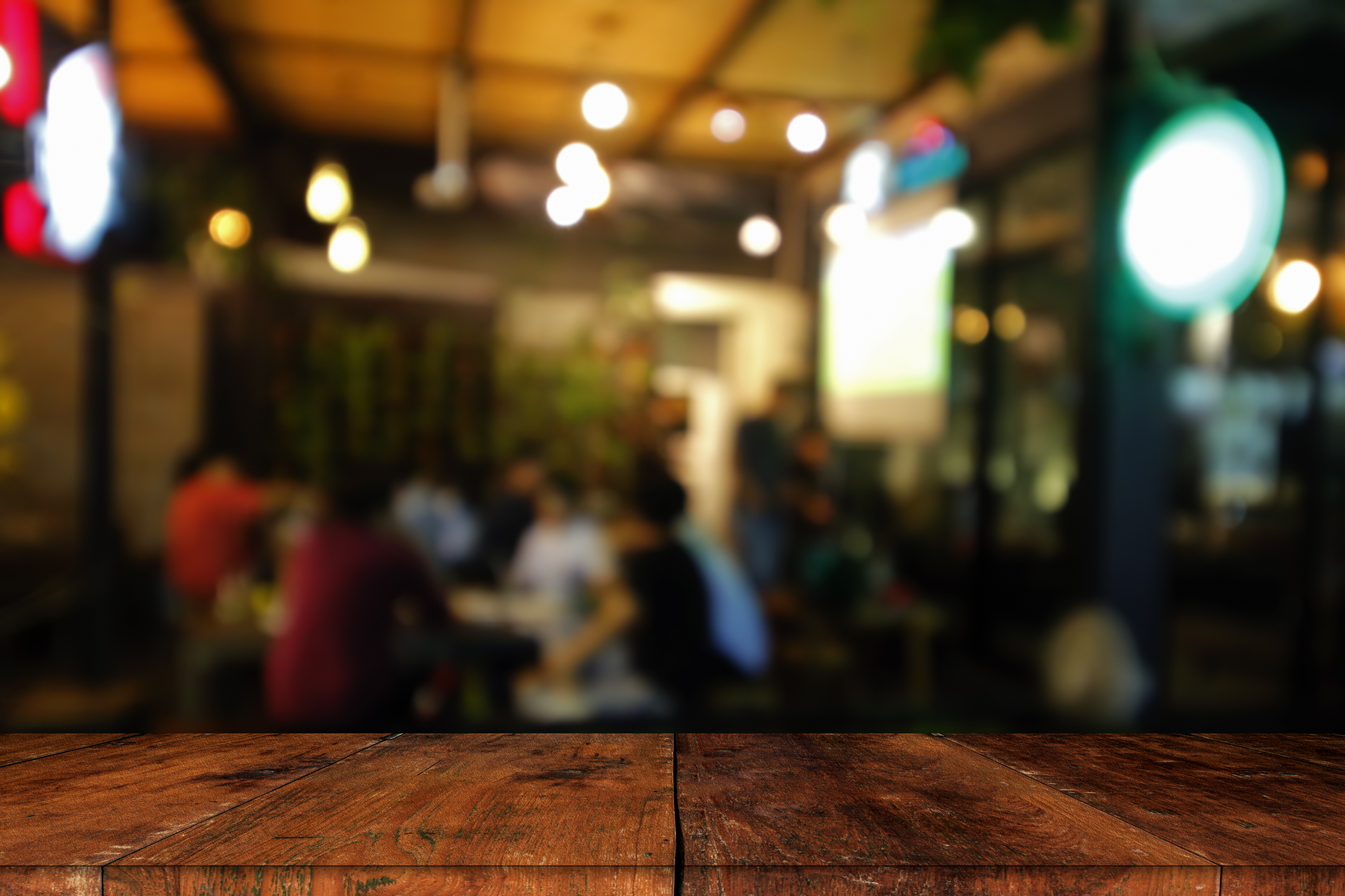 Blurred image of a busy café or restaurant with people socializing and a wooden surface in the foreground