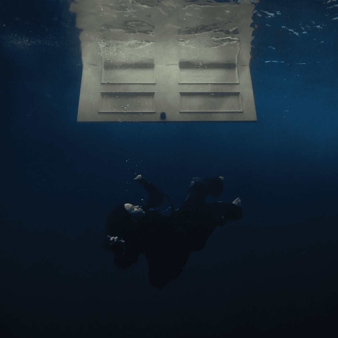 Person underwater beneath a submerged door floating toward the surface