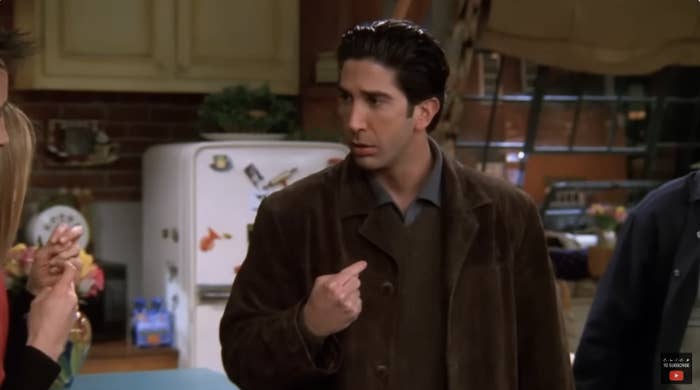 David Schwimmer as Ross Geller pointing at himself in a kitchen scene from Friends. Jennifer Aniston&#x27;s hand is partially visible on the left