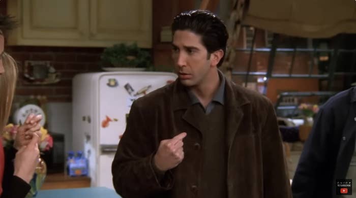 David Schwimmer as Ross Geller pointing at himself in a kitchen scene from Friends. Jennifer Aniston's hand is partially visible on the left