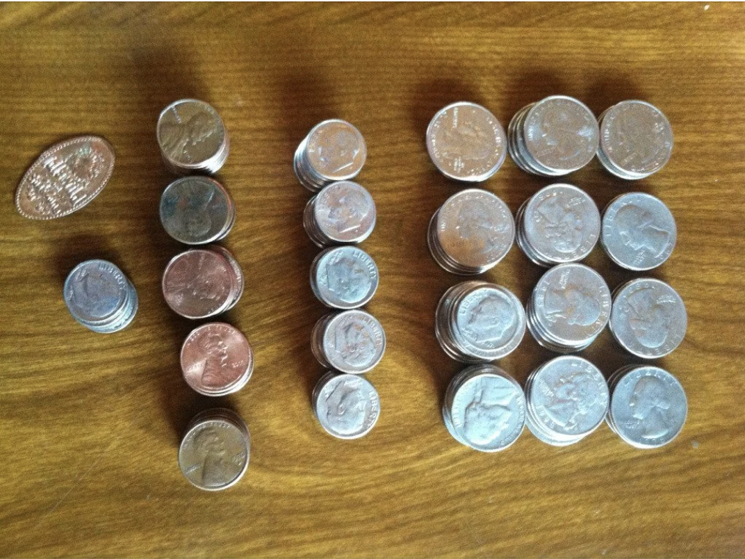 Stacks of various U.S. coins, including pennies, nickels, dimes, and quarters, are organized on a wooden surface