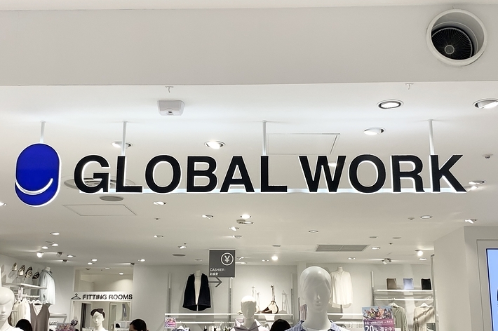 A store with a sign reading &ldquo;Global Work&rdquo; above its entrance. Shoppers browse clothing displays inside