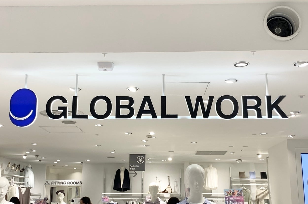 A store with a sign reading "Global Work" above its entrance. Shoppers browse clothing displays inside