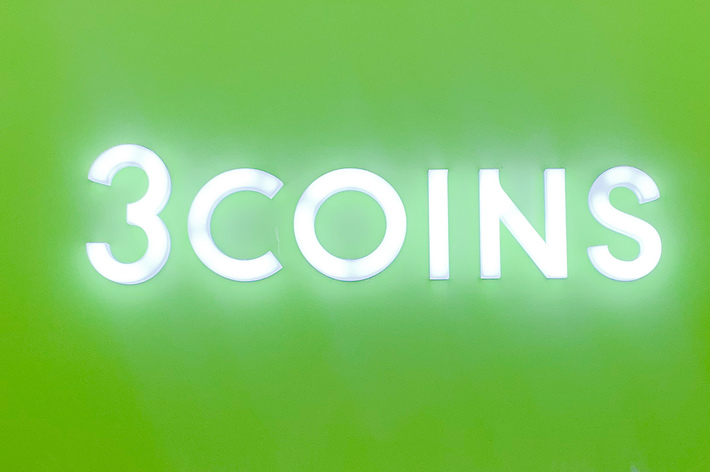 3COINSのロゴが表示された看板。看板の下には商品と3%割引を示すタグが並べられている。