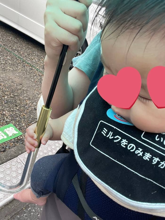 赤ちゃんが傘を持ちながら抱っこされている様子。顔の目の部分がハート型で隠されている。