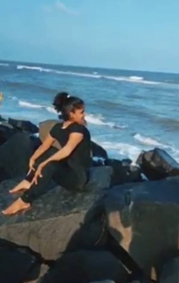 Person doing a seated yoga pose on rocks by the ocean with waves in the background