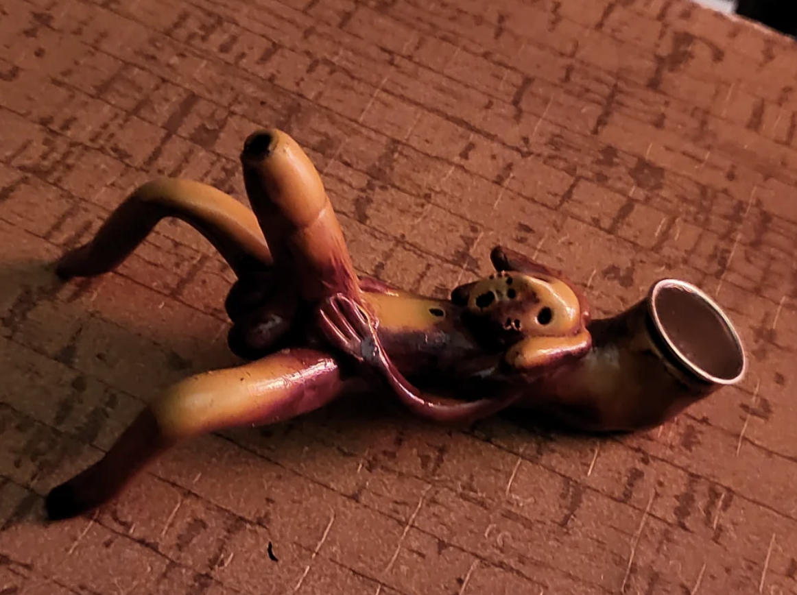A banana-shaped smoking pipe with detailed peel and fruit designs lying on a textured surface