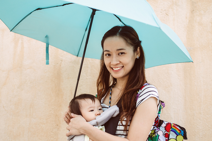 女性が笑顔で赤ちゃんを抱っこ紐で抱え、傘を差している。