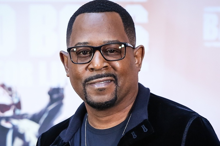 Martin Lawrence smiles on the red carpet, wearing a dark jacket over a t-shirt and glasses, at the premiere of Bad Boys for Life