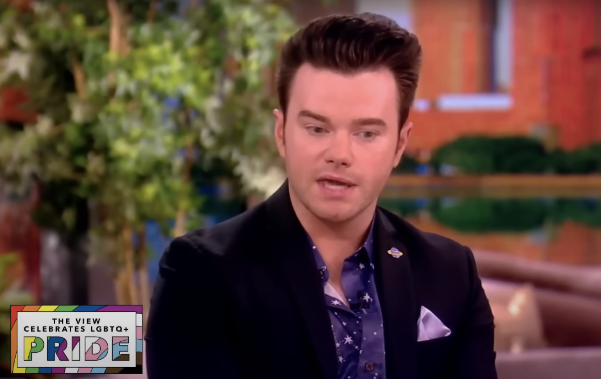 Chris Colfer on &quot;The View&quot; set, discussing LGBTQ+ Pride. He is wearing a dark suit with a patterned shirt and a pocket square. &quot;The View Celebrates LGBTQ+ Pride&quot; displayed in text