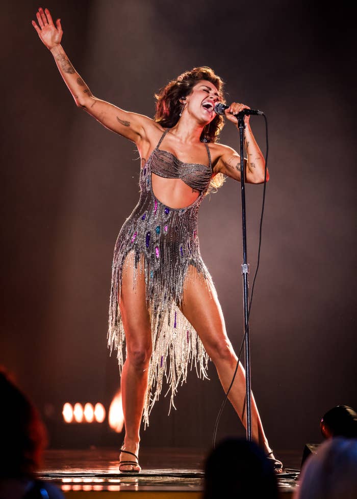 Halsey performs energetically on stage in a glittering, fringe dress with a cutout midriff, singing into a microphone