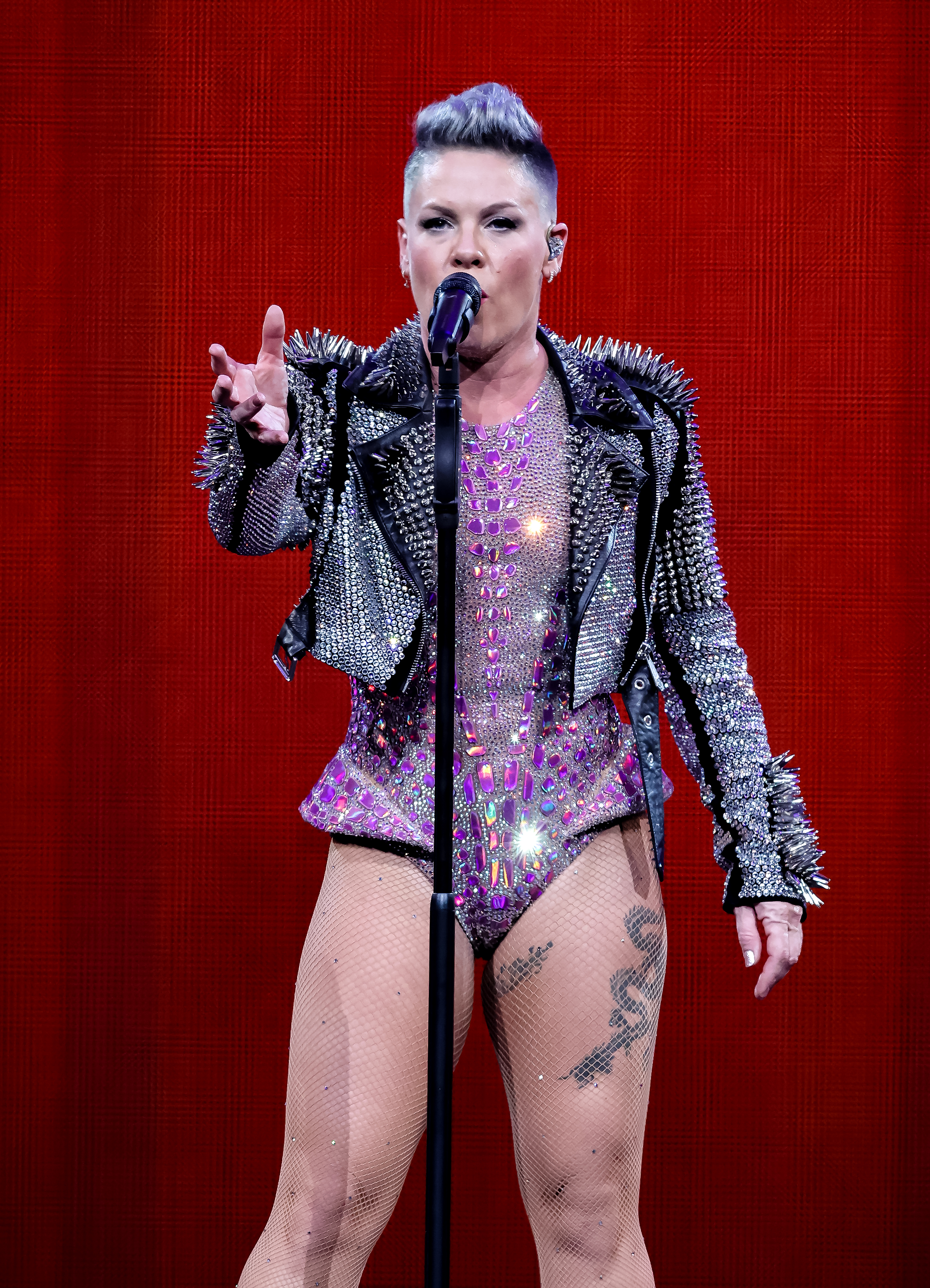 Pink performs on stage in a studded jacket and sequined outfit, singing into a microphone