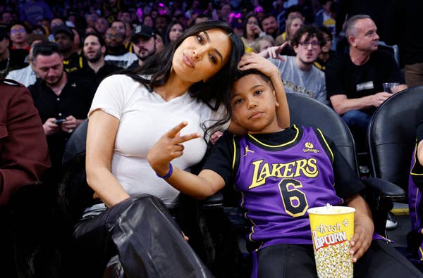 Kim Kardashian and Saint West sit courtside at a basketball game. Kim is dressed casually, and Saint wears a Lakers jersey, holding popcorn