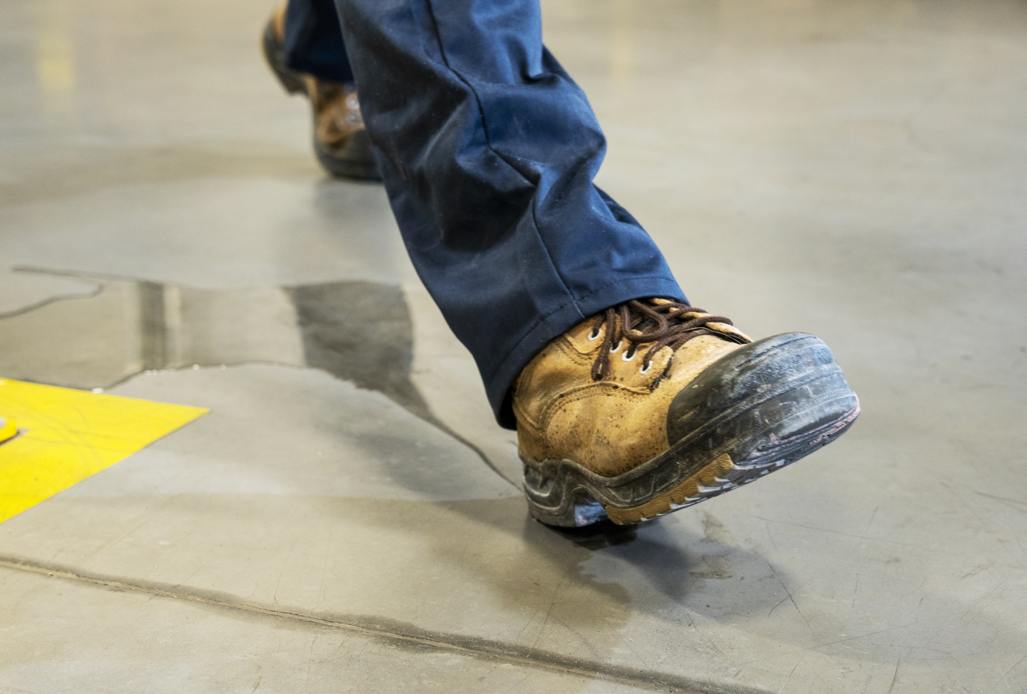 A person wearing work boots and blue pants slips on a wet floor in an industrial setting