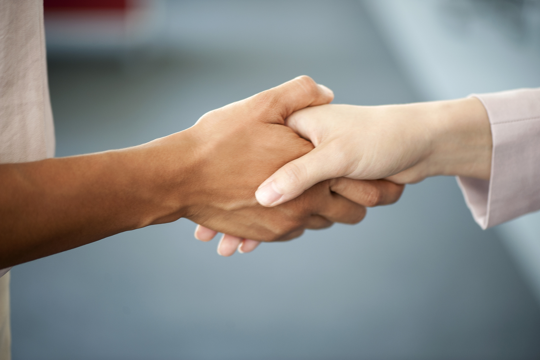 Two people shaking hands, focusing on the hands and forearms. One person has a light skin tone and the other has a darker skin tone