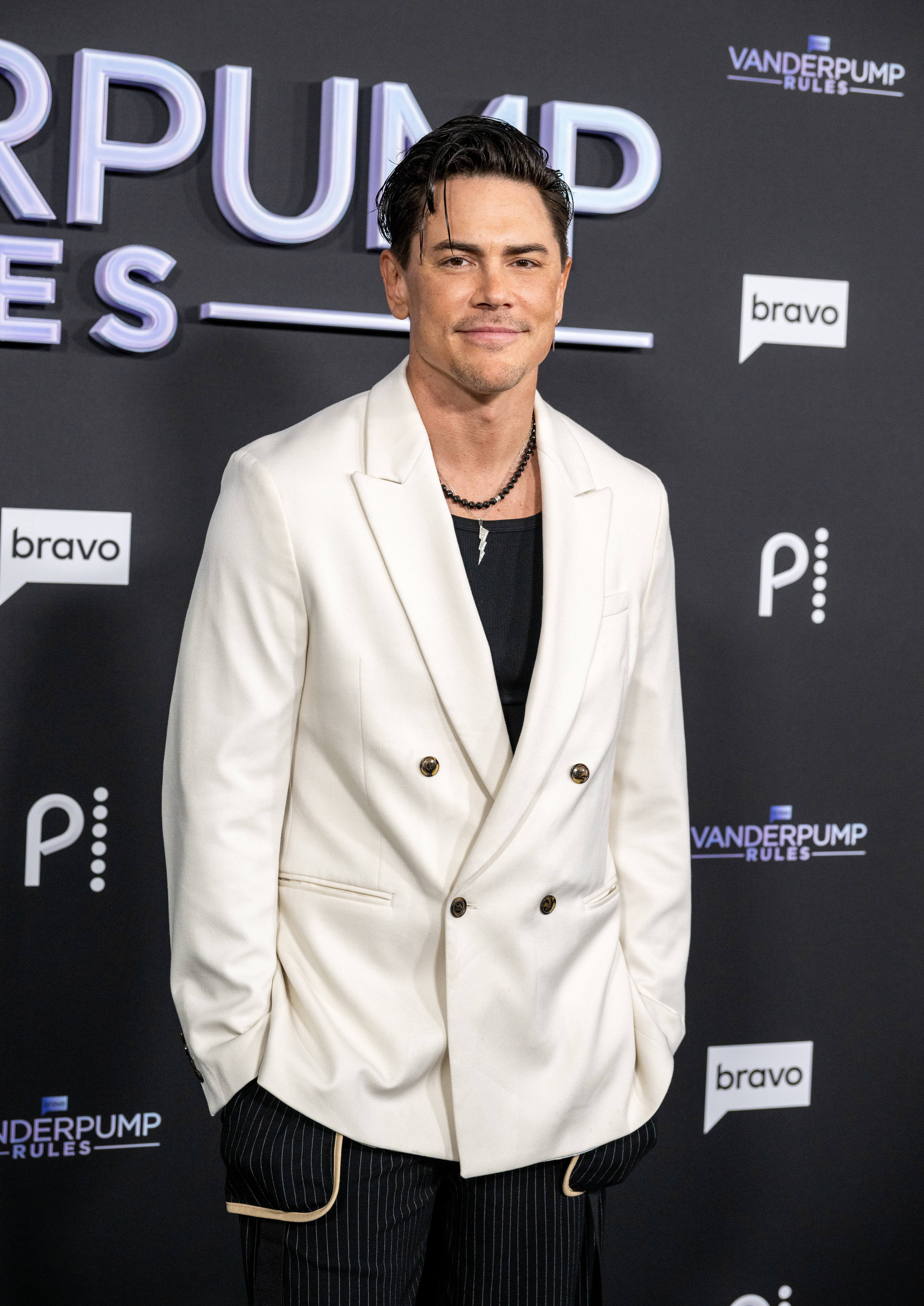 Tom Sandoval poses on the Vanderpump Rules red carpet in a white double-breasted blazer over a black shirt, paired with pinstripe pants