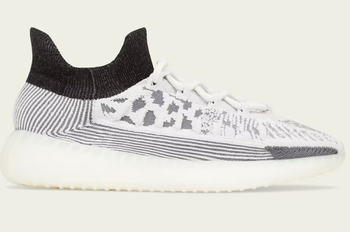 Side view of a modern knit sneaker with a sleek, sock-like design and intricate patterns that resemble abstract art. The shoe features a thick, cushioned sole