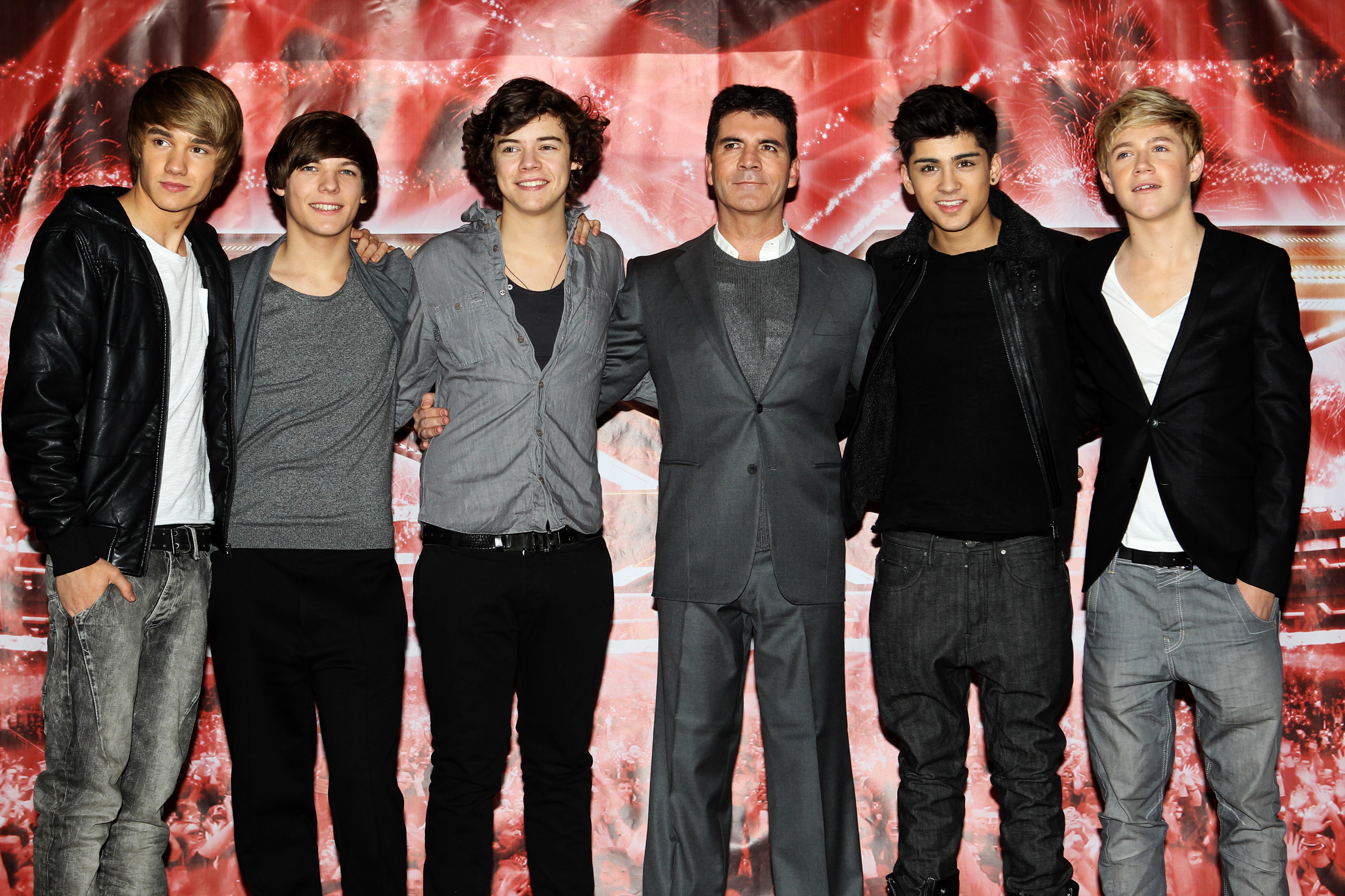 Liam Payne, Louis Tomlinson, Harry Styles, Simon Cowell, Zayn Malik, and Niall Horan stand together on a red carpet. The band members sport casual outfits; Cowell is in a suit