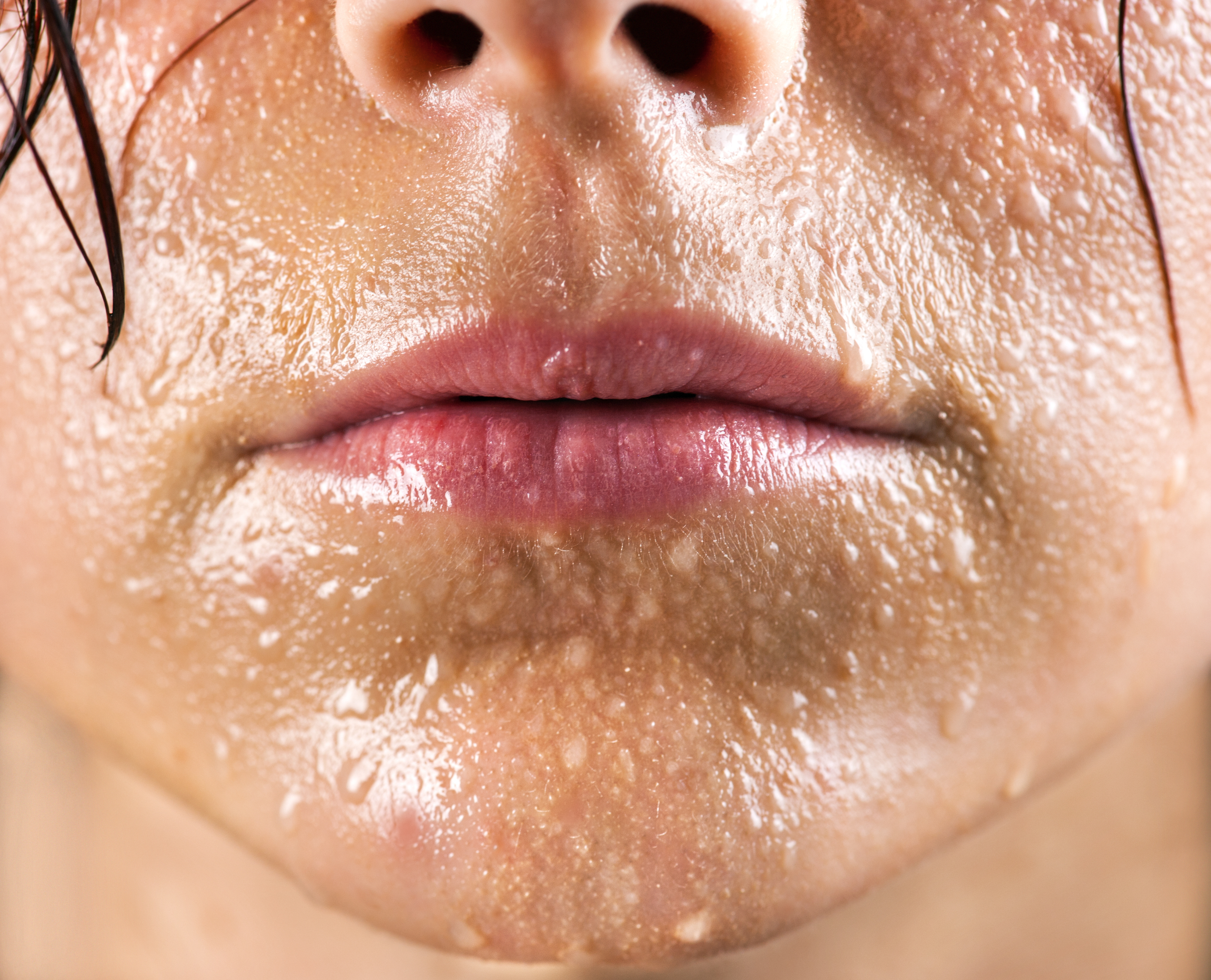 Close-up image of a person's face with sweat prominently visible on their skin