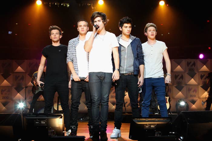 Louis Tomlinson, Liam Payne, Harry Styles, Zayn Malik, and Niall Horan of One Direction perform on stage, all wearing casual outfits with jeans and shirts