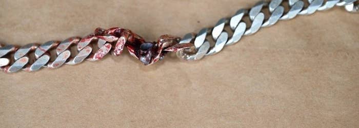 Close-up of a silver chain with one link stained with blood and damaged, suggesting it has been tampered with or forced apart