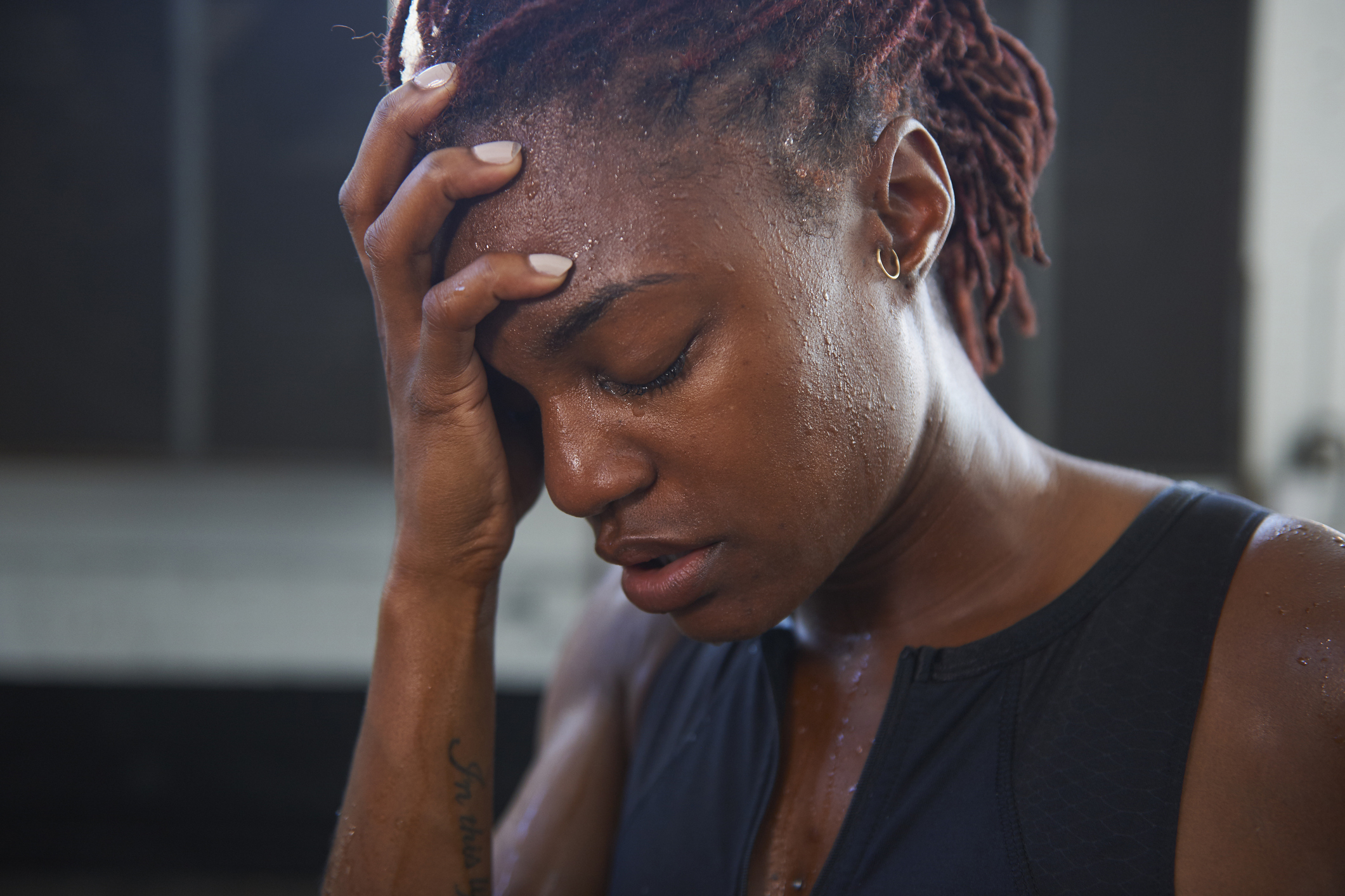 Person with braided hair resting their hand on their forehead, sweating, and appearing exhausted, possibly after a workout or strenuous activity