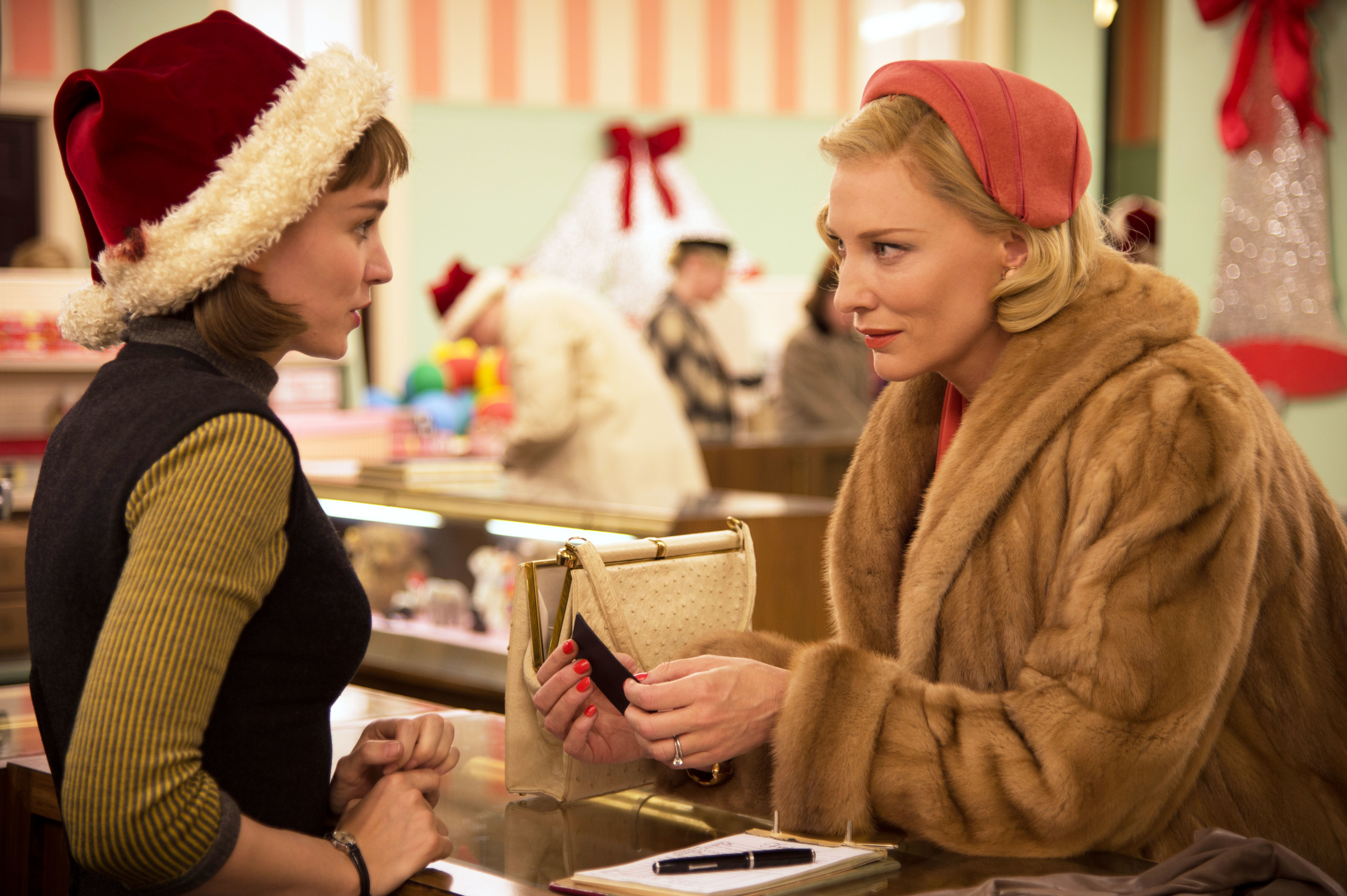 Rooney Mara and Cate Blanchett in a shopping scene from &quot;Carol,&quot; discussing over a purse on a counter. Rooney wears a Santa hat; Cate is in a fur coat