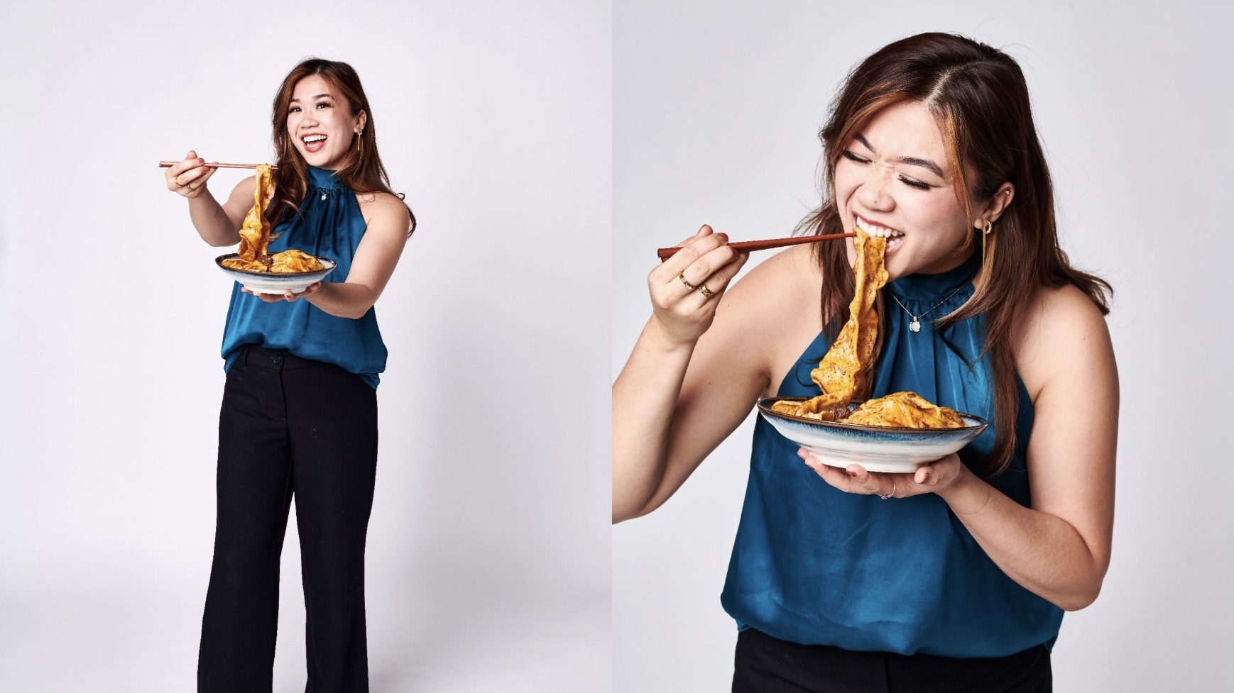 Woman in a blue sleeveless top and black pants enthusiastically eating noodles with chopsticks, holding a full plate of food