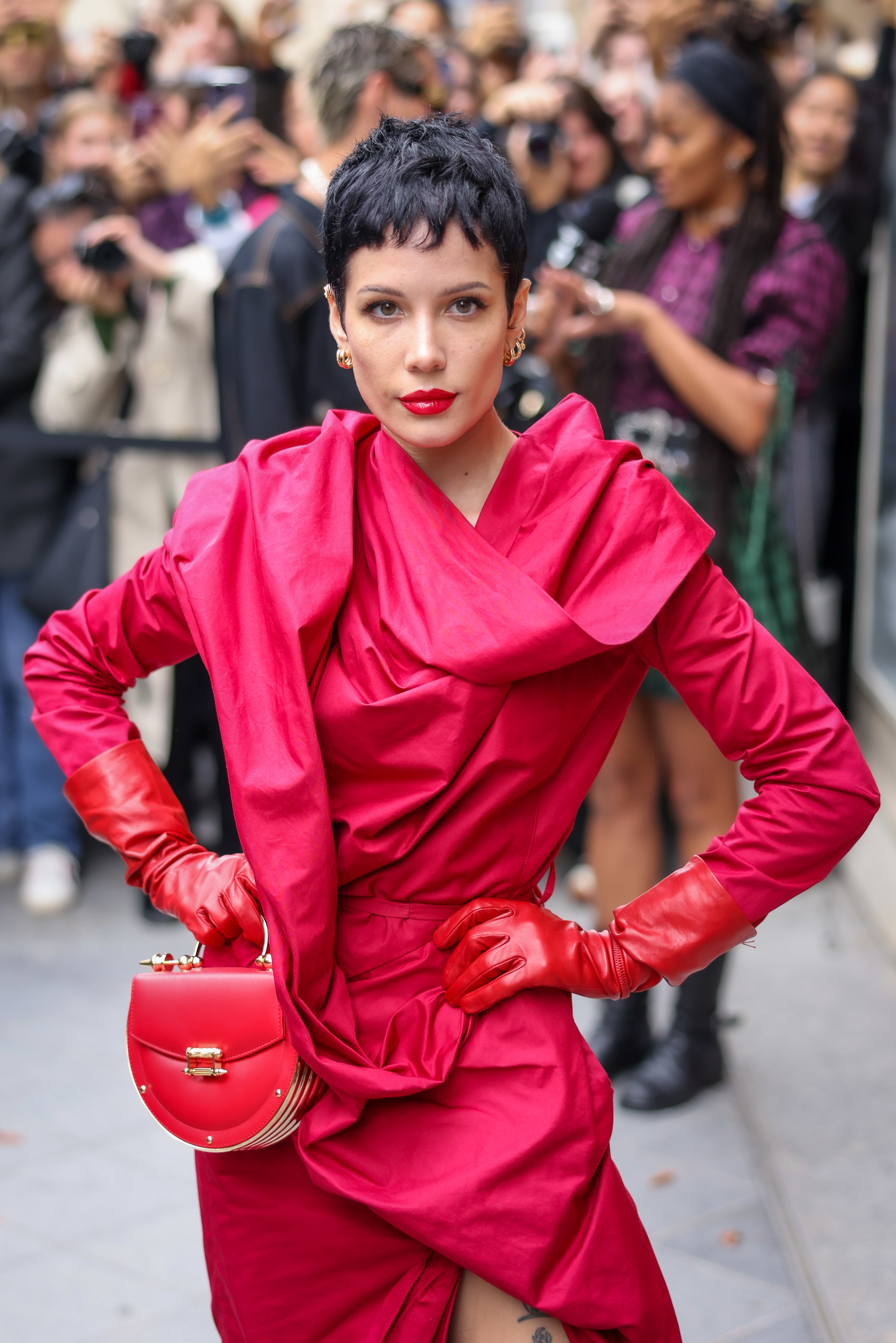 Halsey is wearing an avant-garde outfit with gloves and holding a matching handbag, posing for photos at a public event