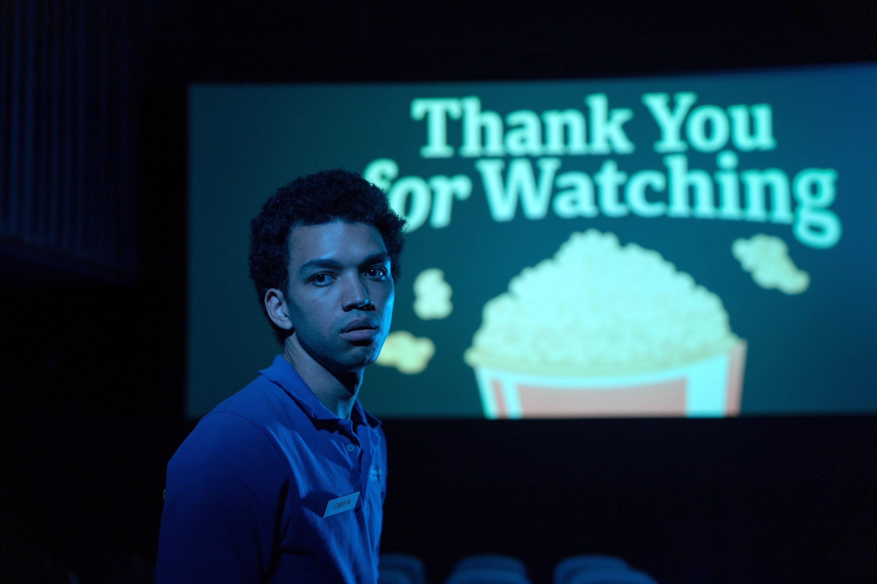 A young man in a blue shirt stands in front of a movie screen that says &quot;Thank You for Watching&quot; with an image of popcorn