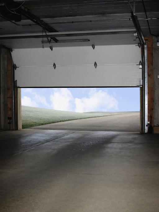 Open garage door revealing a scenic view of a green hill and blue sky with clouds