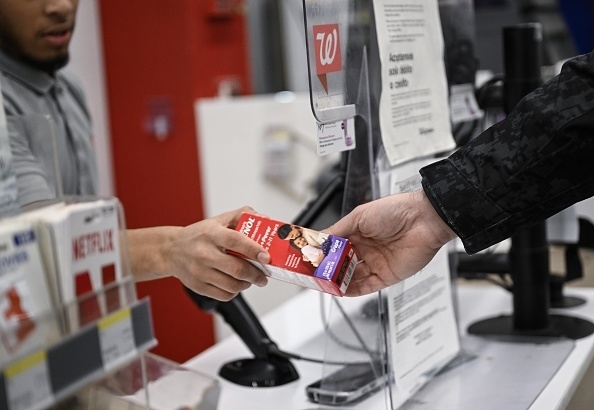 A person hands a box of Plan B emergency contraceptive pills to a cashier at a checkout counter in a store