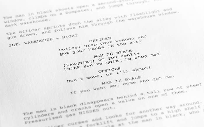 Close-up of a movie script page showing dialogue between an officer and a man in black, with stage directions marking a night scene in a warehouse