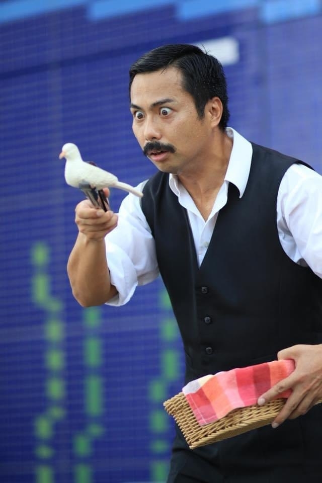 男性が一羽の白い鳩を指に乗せて話しかけている。彼は白いシャツに黒いベストとズボンを着ている。