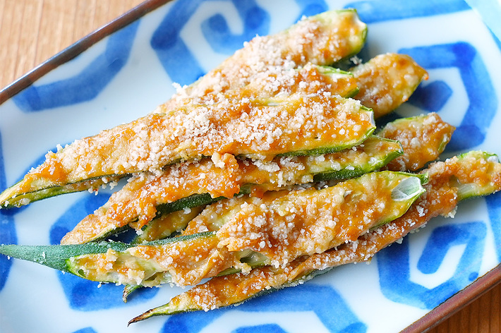 木製テーブルに置かれた模様入りの皿に盛られた料理。揚げたズッキーニがパン粉をまとい、並べられている。