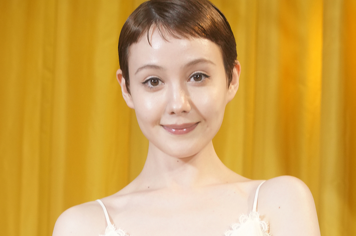 女性が白いドレスを着ている姿。背景は黄色いカーテン。