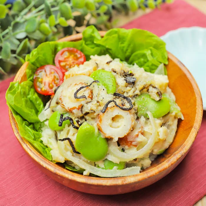 木のボウルに入ったポテトサラダには、トマト、レタス、そら豆、玉ねぎ、ちくわがトッピングされています。