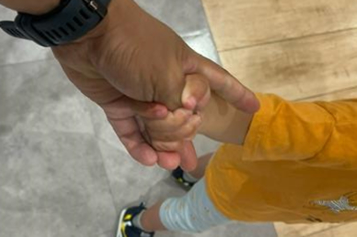 大人が子供の手をしっかりと腕時計越しに掴んでいる写真。テキストには「無理に子供の手首を掴むのではなく子供に親指を握ってもらうようにする」とあります。