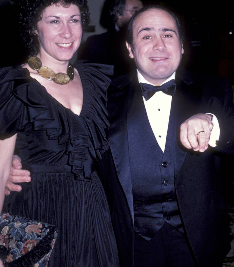 Danny DeVito in a tuxedo, posing with Rhea Perlman in a evening gown with a large necklace at an event