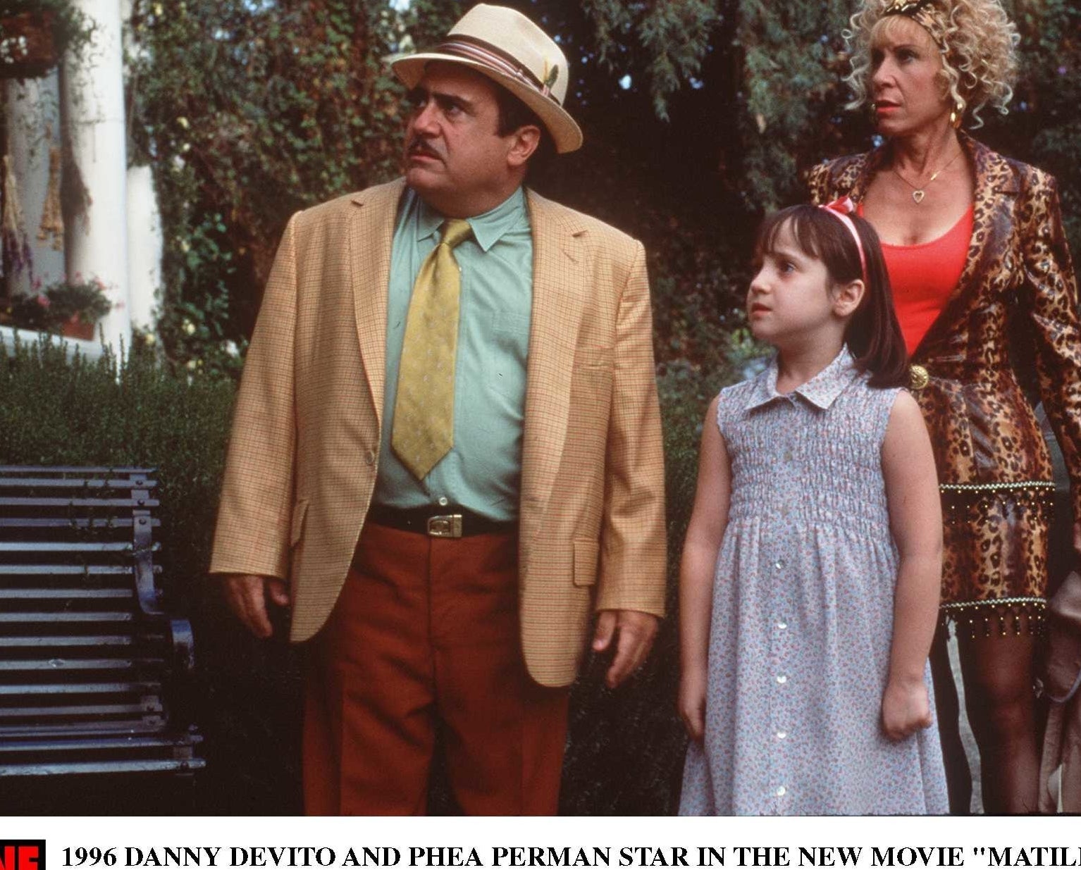 Danny DeVito and Rhea Perlman stand outdoors looking surprised alongside Mara Wilson who played Matilda