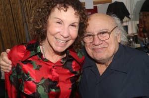 Rhea Perlman and Danny DeVito smiling together, with Rhea wearing a floral patterned shirt and Danny in a casual button-up