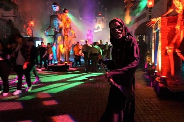 People walk through a spooky, dimly lit Halloween-themed attraction featuring skeletal figures and eerie lighting
