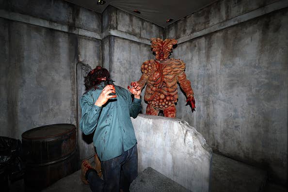 A person in tattered clothing appears frightened and cowers in front of Demogorgon, a monstrous, humanoid creature from "Stranger Things," in a dim, dungeon-like setting