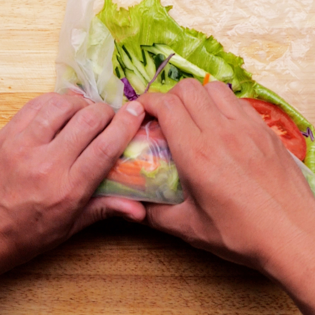 人が野菜をライスペーパーで巻いている様子。