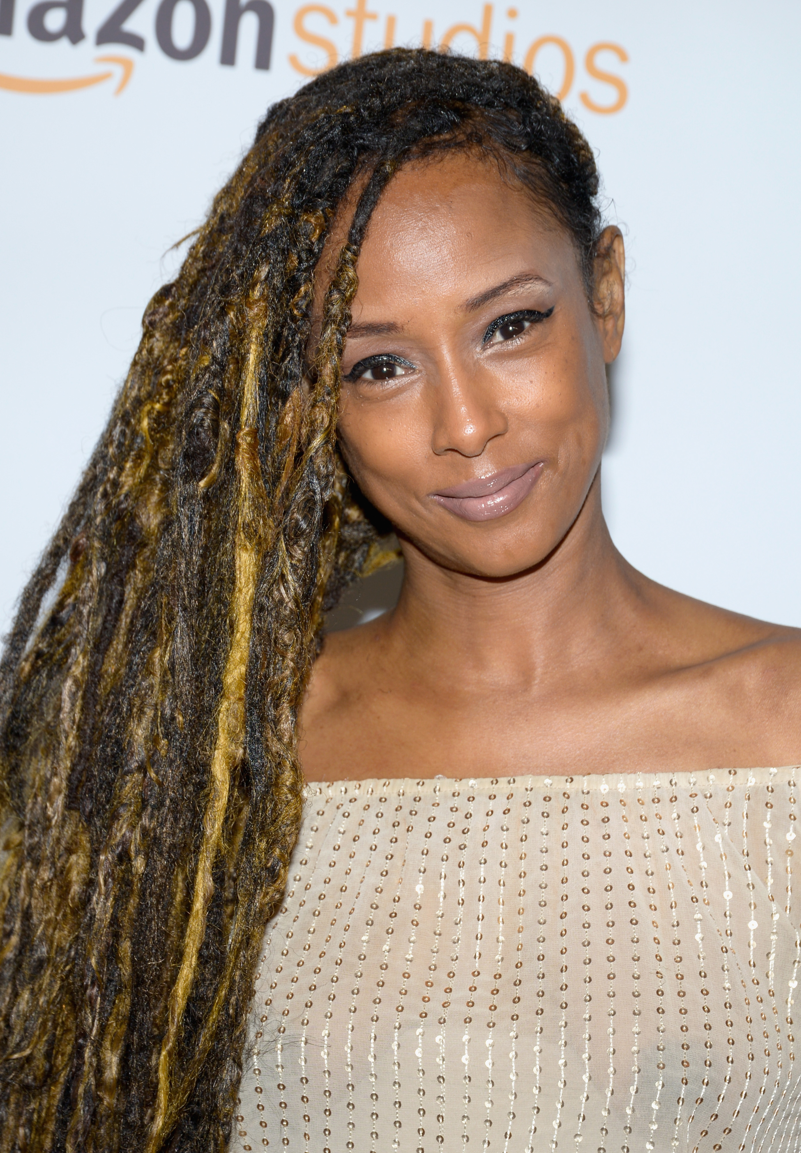 New York Fashion Week: Kelsey Scott in an off-shoulder, beige dress with long, highlighted dreadlocks, poses on the red carpet against an Amazon Studio backdrop