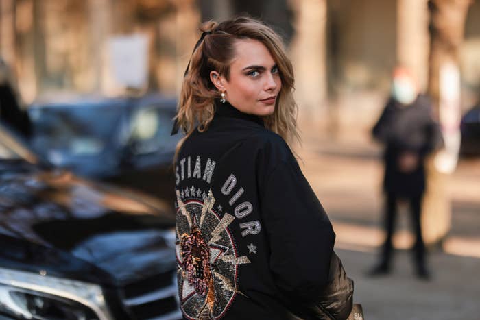 Cara Delevingne, wearing a Christian Dior jacket outdoors, looking over her shoulder at the camera